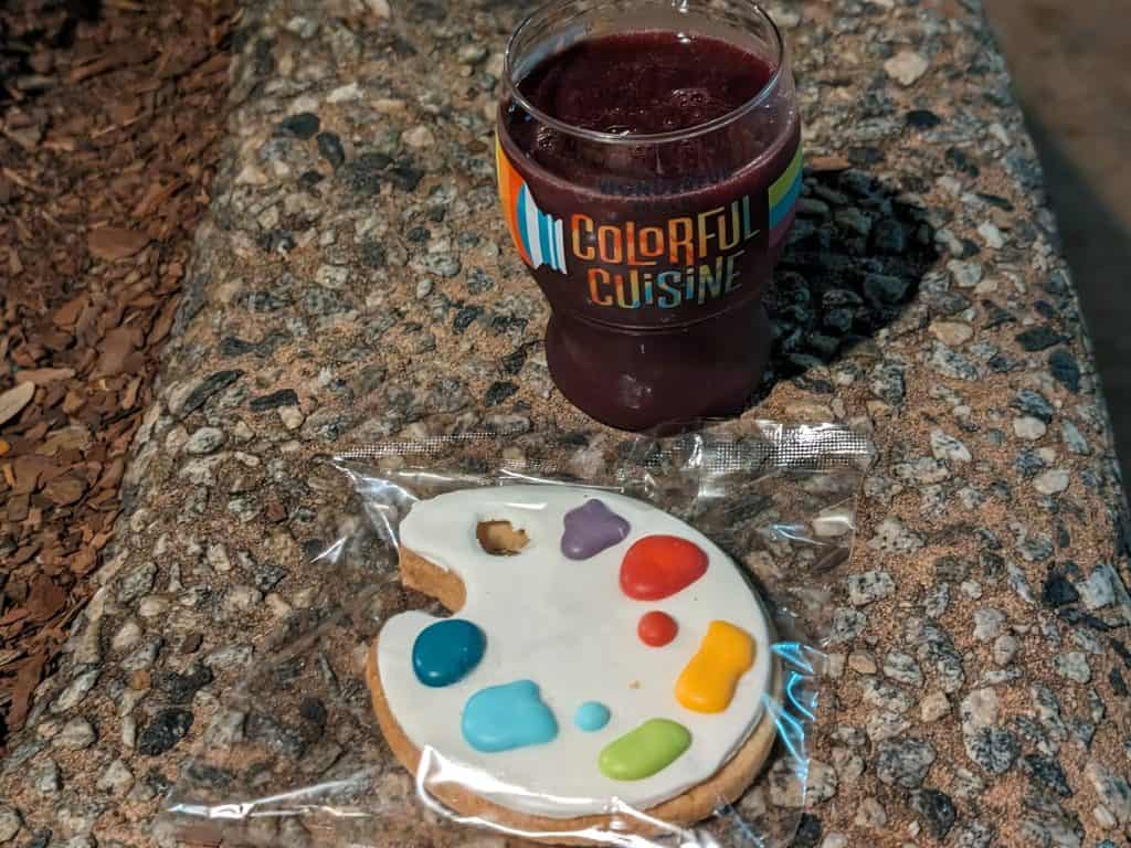 Wildberry Smoothie in a decorative plastic glass next to a sugar cookie shaped like an artist palette with dabs of colorful icing meant to look like paint