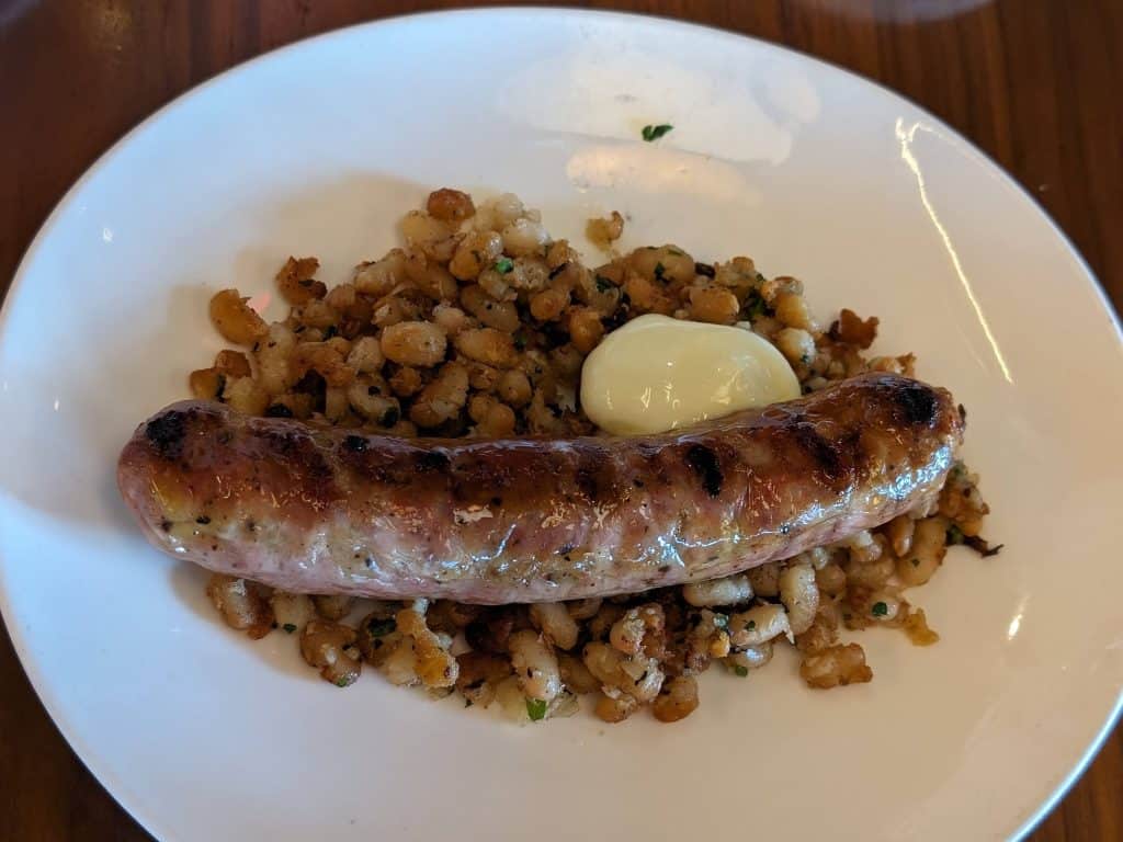 A pork sausage plated on top of sauteed white beans with aioli