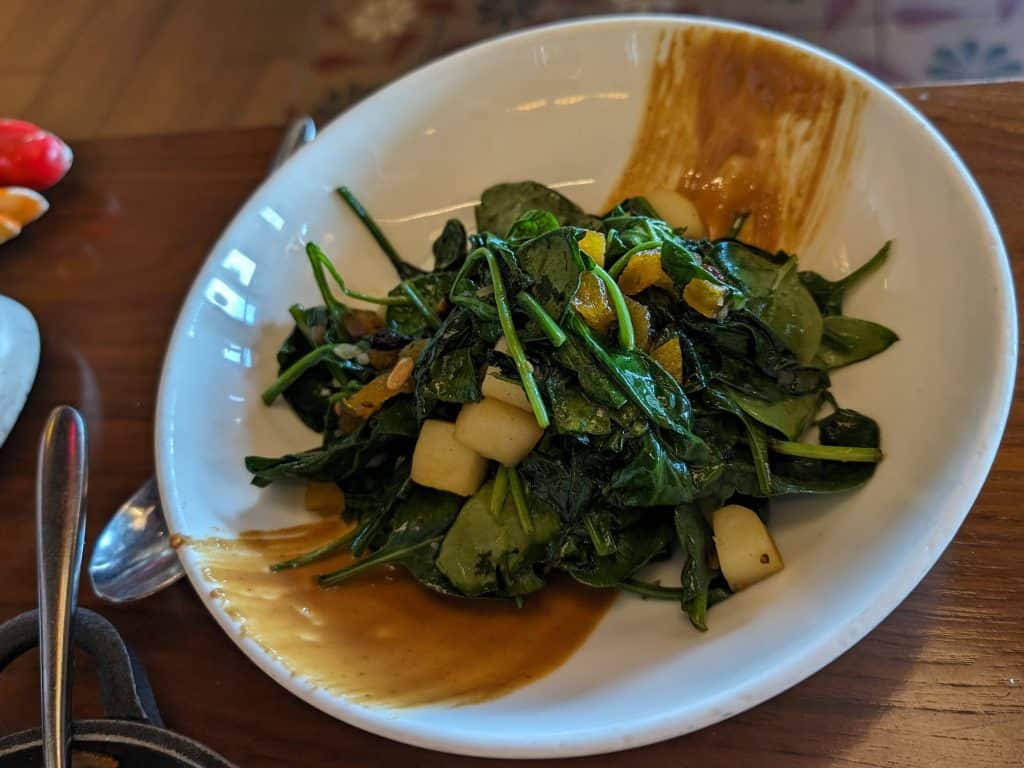 Cooked spinach with pine nuts, apples, and raisins with a peanut sauce