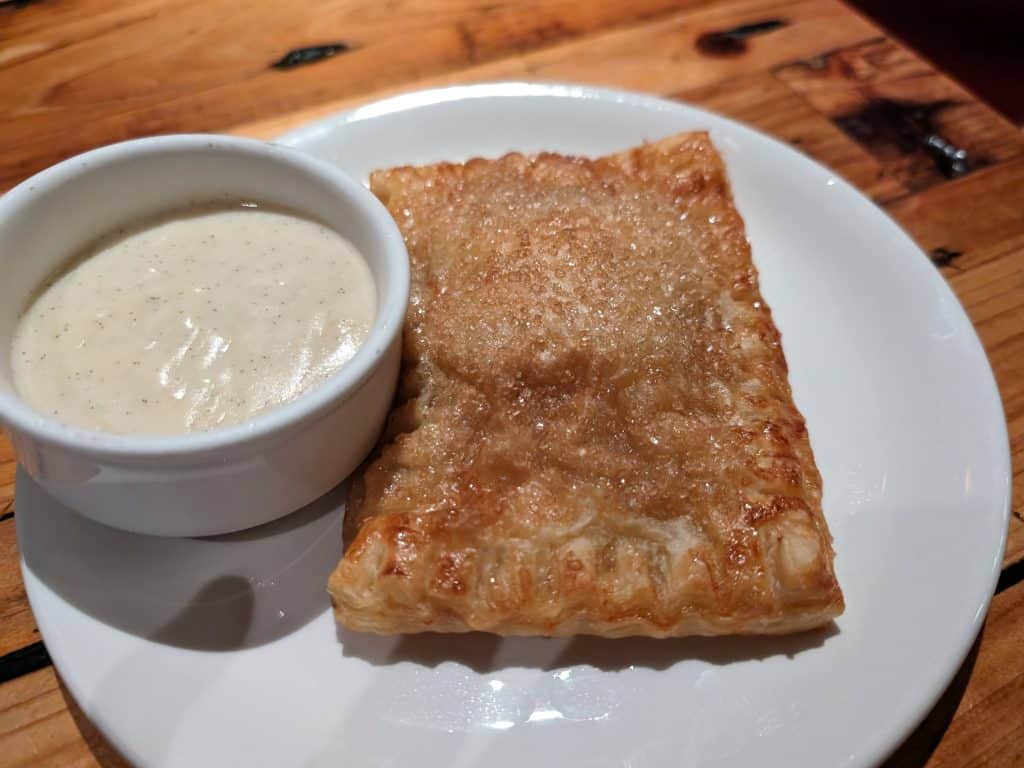 Apple strudel on a plate with a small bowl of vanilla cream sauce