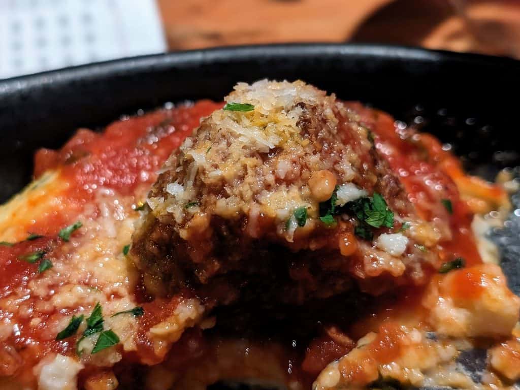 A meatball topped with sauce and cheese in a cast iron dish