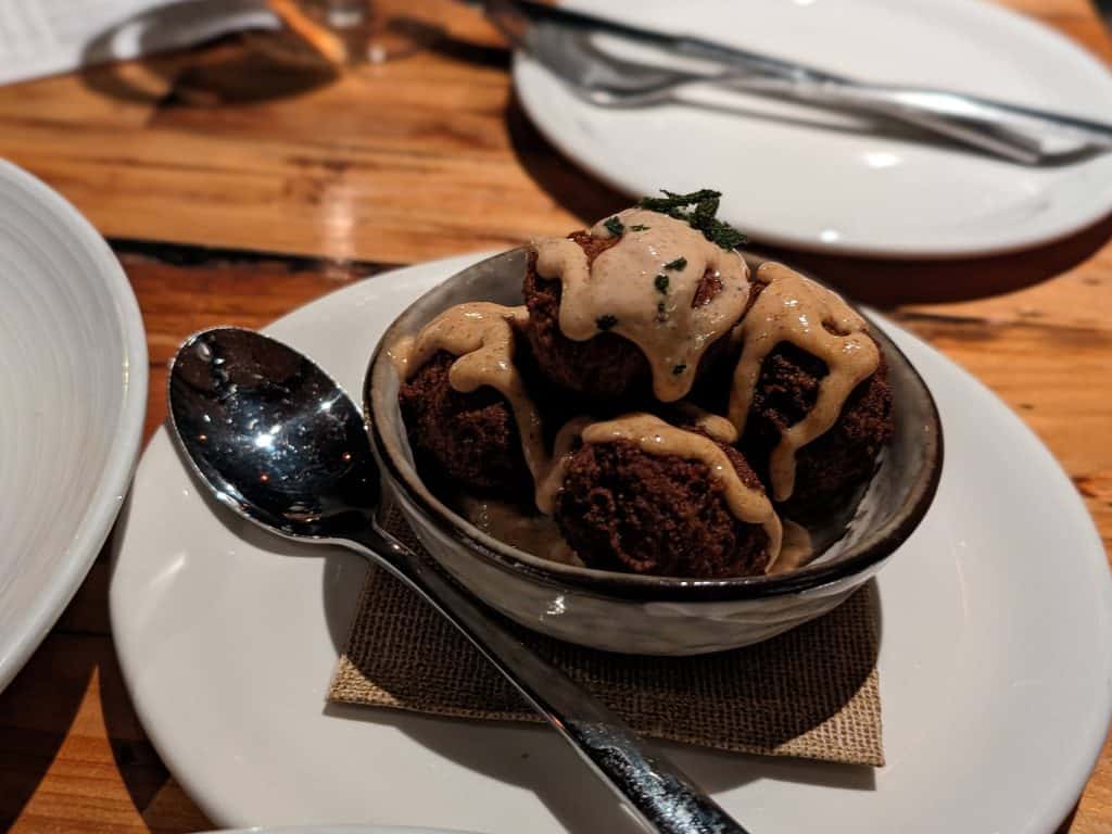 Bowl filled with Pumpkin Fritters drizzled with a bacon brown butter aioli and topped with fried sage