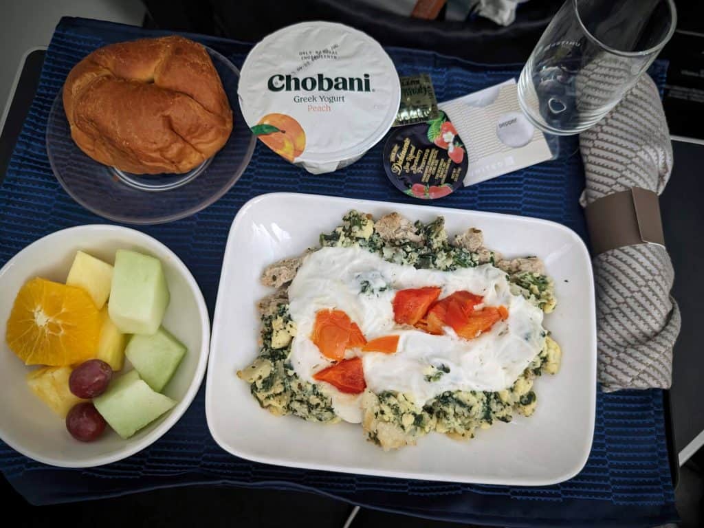 Chicken and Spinach Egg Scramble on an airplane food tray with a croissant, yogurt, and fresh fruit