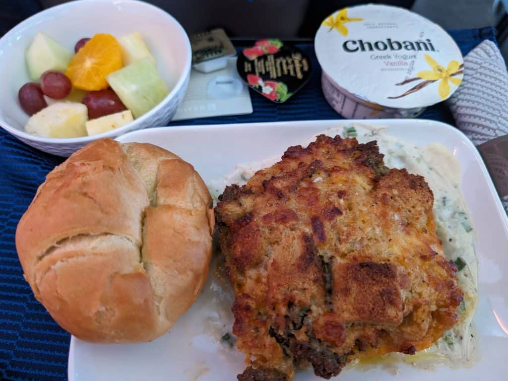 An airplane breakfast on a tray consisting of a Sausage and Cheddar Souffle on an Herbed Cream Sauce with a Croissant