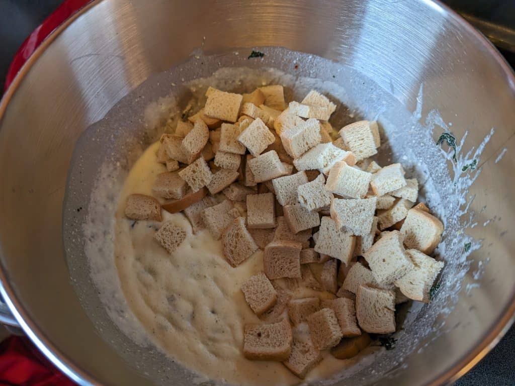 Adding dried keto bread cubes to an egg and cream mixture