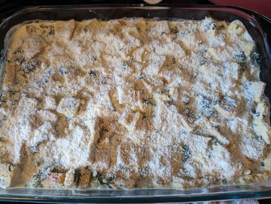 Topping Keto Florentine Breakfast Strata with grated Parmesan Cheese before baking