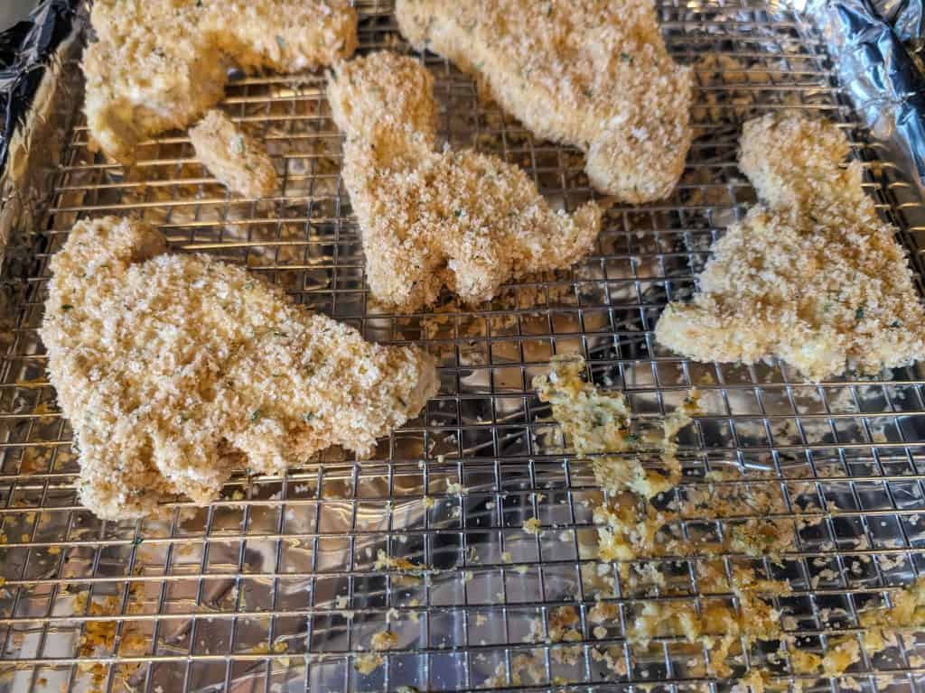 Breaded but not yet baked Gluten-Free Dinosaur Chicken Patties on a wire rack on a baking sheet