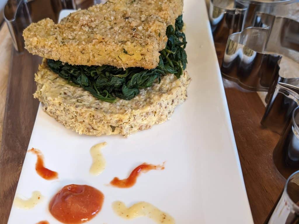 Gluten-Free Dinosaur Chicken Patty on top of Sautéed Garlicky Spinach and a Ranch Cauliflower Chia Cake on a plate from a side angle