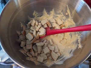 Adding keto bread cubes into the wet mixture for Keto Gruyere Bread Pudding