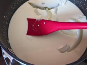 Cooking Keto Mornay Sauce in a saucepan before straining out the aromatics