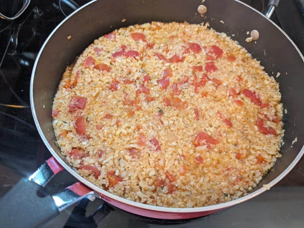 Cooking cauliflower rice and canned diced tomatoes in a pan with chicken stock