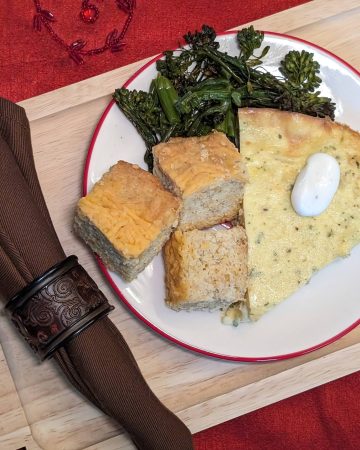 A wedge of Crustless Broccoli and Blue Cheese Quiche on a plate with Keto Cheese Bread and Garlic Roasted Broccolini
