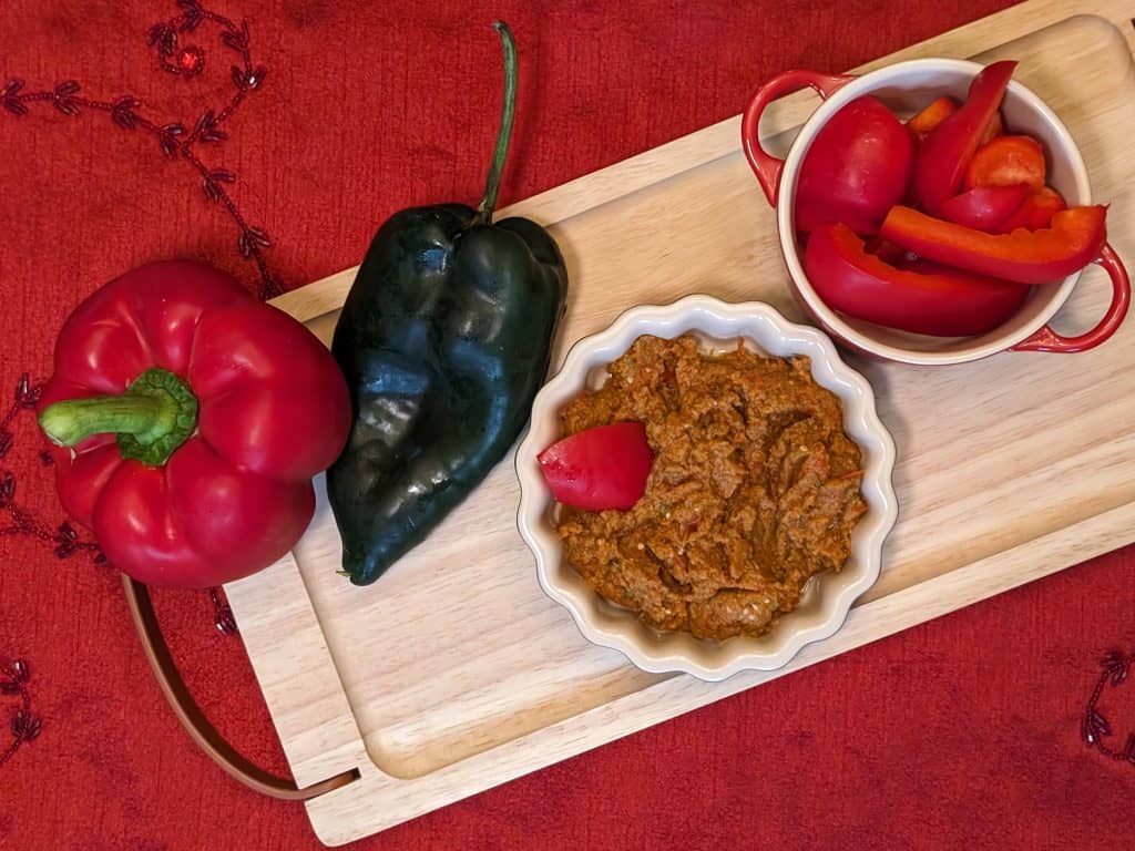 Harissa Veggie Spread in a serving dish next to sliced red bell pepper dippers and a whole red bell pepper and poblano pepper