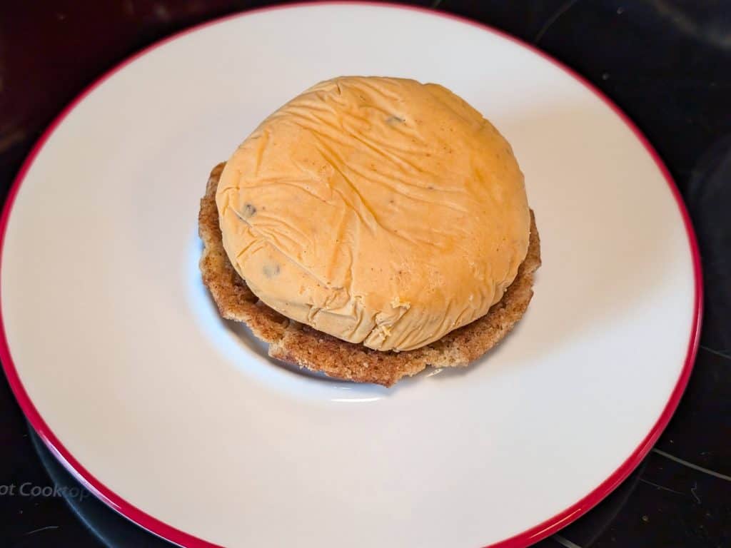 A plate with a frozen disk of Chipotle Keto Ice Cream on top of an upside down Keto Snickerdoodle Cookie as the 3rd step in constructing a Keto Chipotle Ice Cream Sandwich