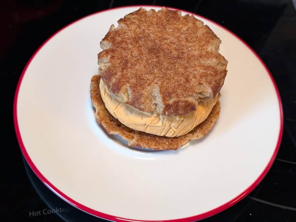 A plate with a frozen disk of Chipotle Keto Ice Cream between two Keto Snickerdoodle Cookies as the 4th step in constructing a Keto Chipotle Ice Cream Sandwich