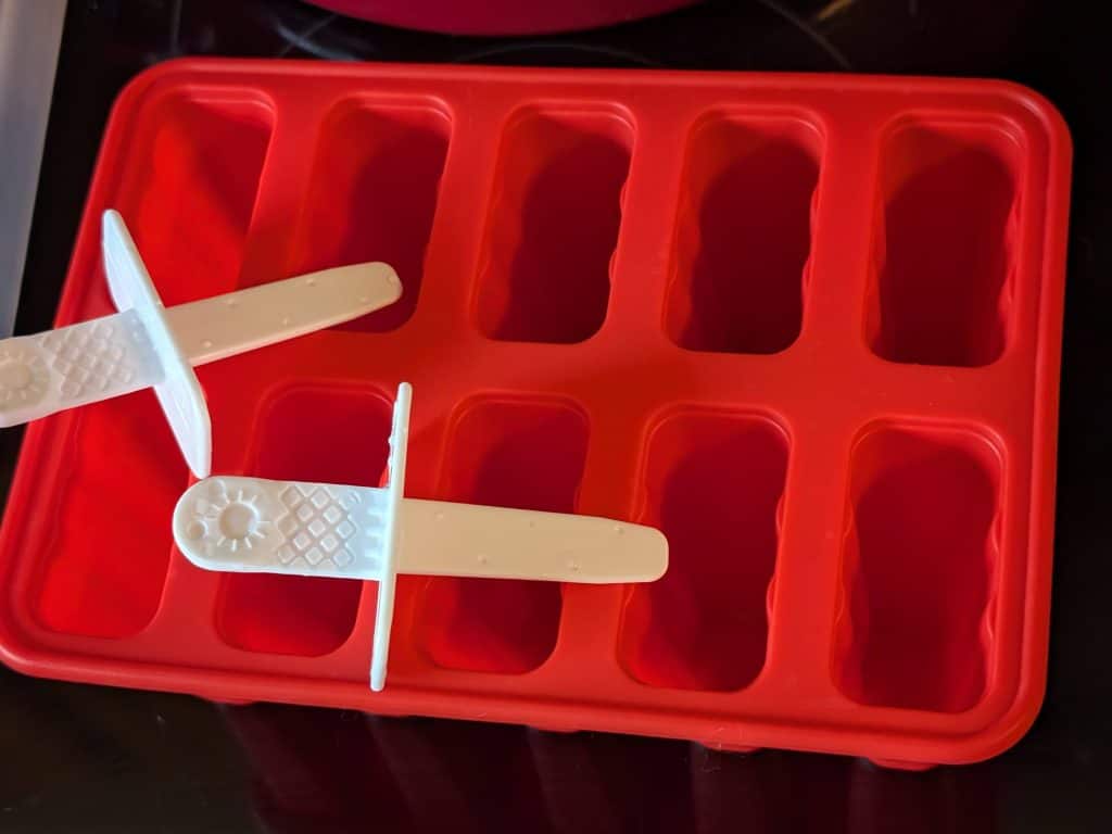 An empty 10 cavity silicone popsicle mold with 2 of its associated popsicle sticks