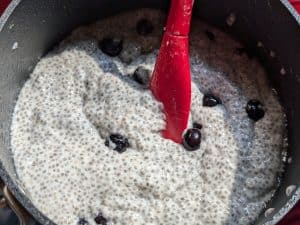 Stirring the blueberries into a saucepan with the mixture for Creamy Keto Fruit Popsicles