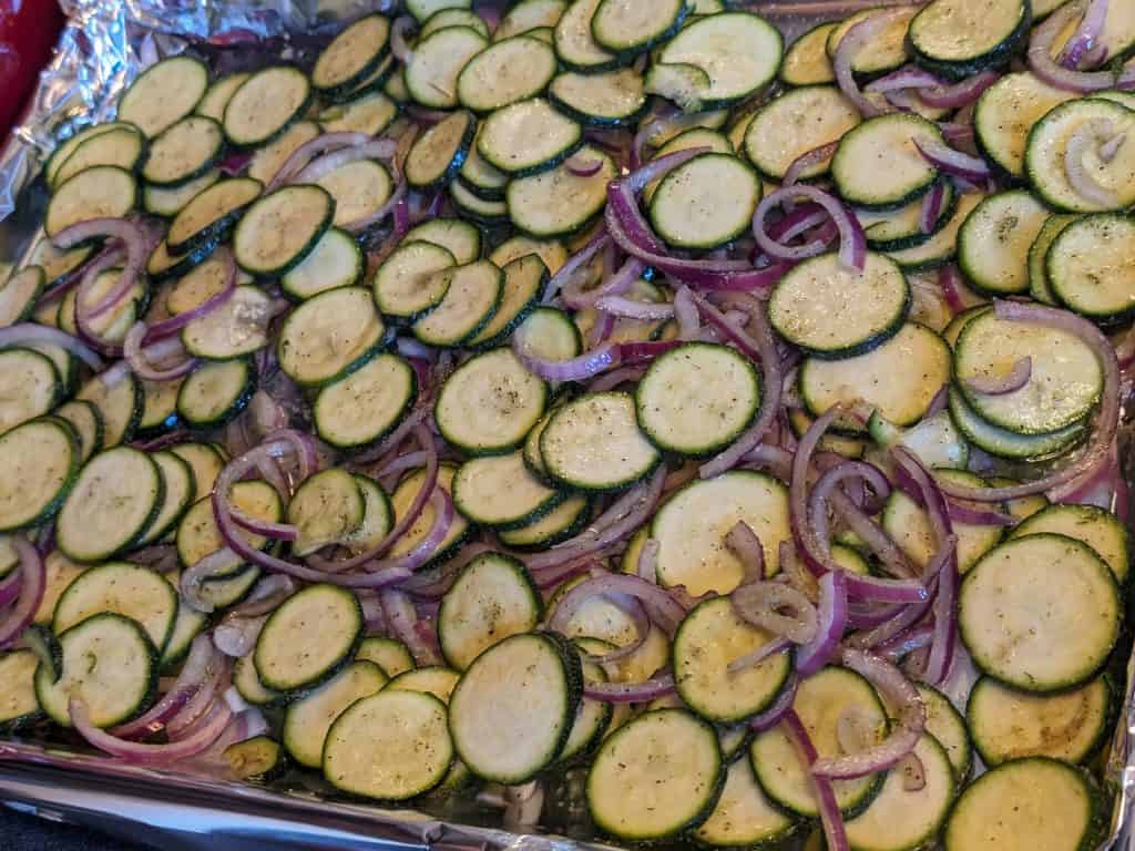 Sliced zucchini and red onion on a sheet pan ready to roast