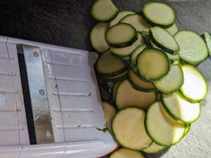 Slices of zucchini on a cutting board with a mandolin slicer