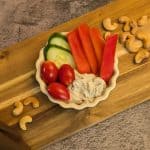 Creamy Za'atar Cashew Dip in a dish with slices of cucumber, red bell pepper, and grape tomatoes with some cashews on the side