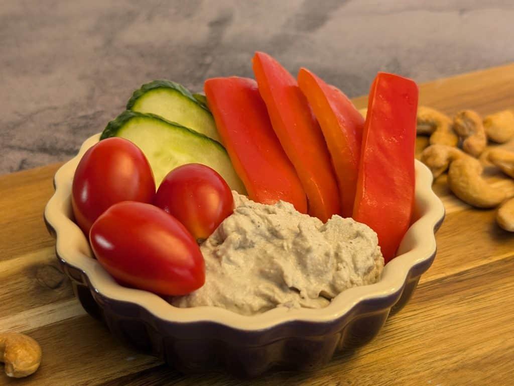 Creamy Za'atar Cashew Dip in a dish with slices of cucumber, red bell pepper, and grape tomatoes