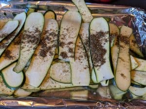 Long zucchini slices on a baking sheet being seasoned with Za'atar and Spring Salt