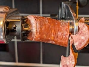 A chunk of smoked sausage being spiralized on a stand mixer