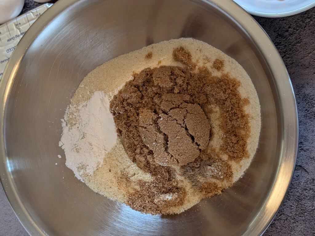 Mixing bowl containing almond flour, brown sweetener, baking powder, nutmeg, and cardamom