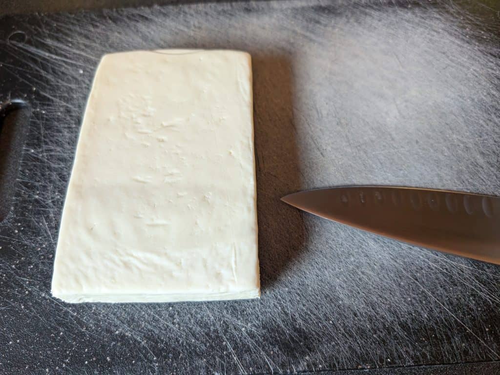 Block of Paneer on a cutting board next to a chef's knife