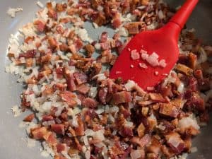 Combining cooked bacon pieces and sauteed onions in pan