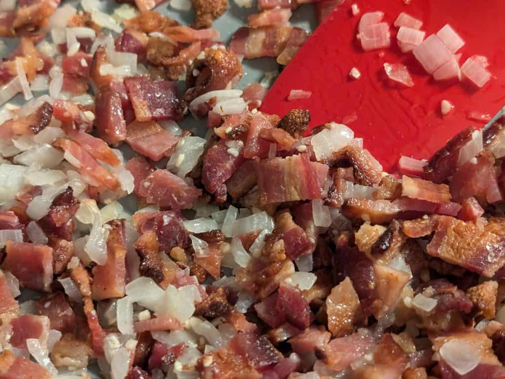 Combining cooked bacon pieces and chopped sauteed onions in pan - close-up