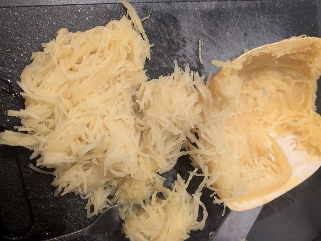 Shredded a roasted spaghetti squash that has been cut in half with the seeds removed