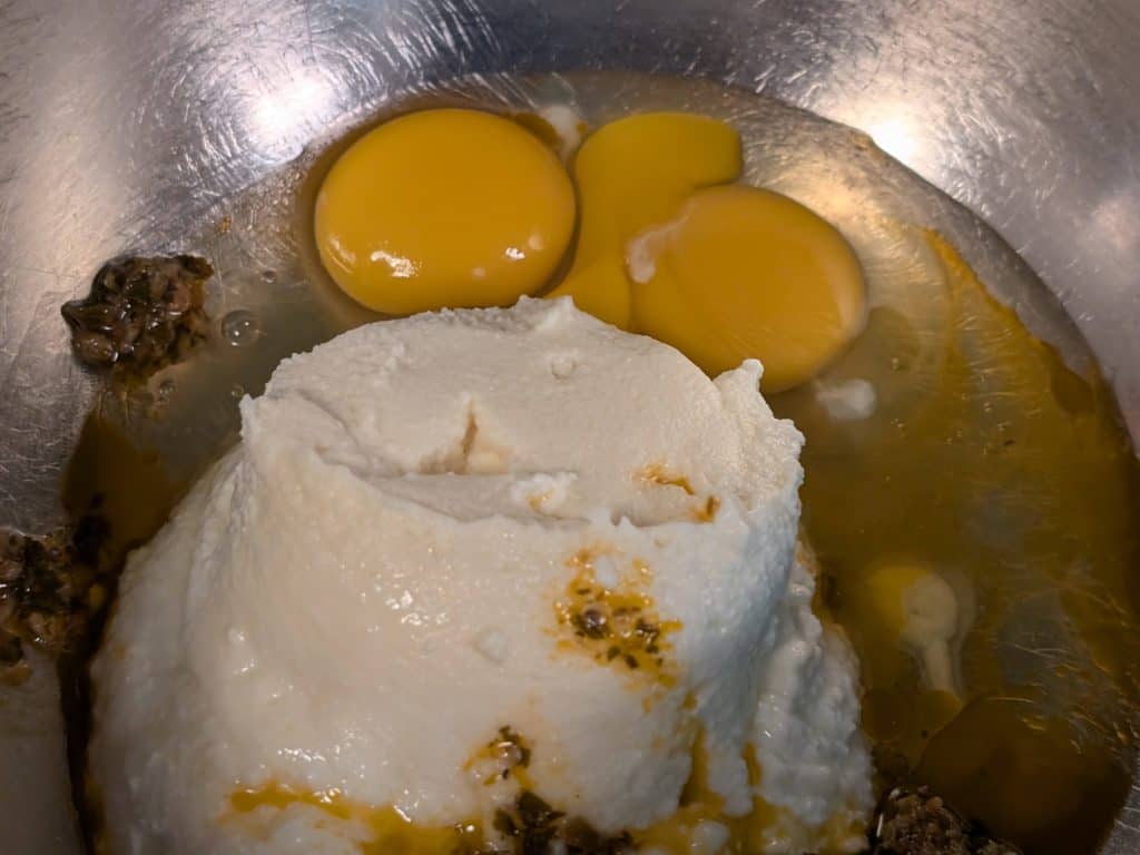 Ricotta cheese, raw eggs, and The Blonde Italian Garlic Dipping Sauce in a bowl, ready to mix