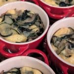 Individual sized Zucchini Gouda Bakes already baked in coquettes set on a rimmed baking sheet