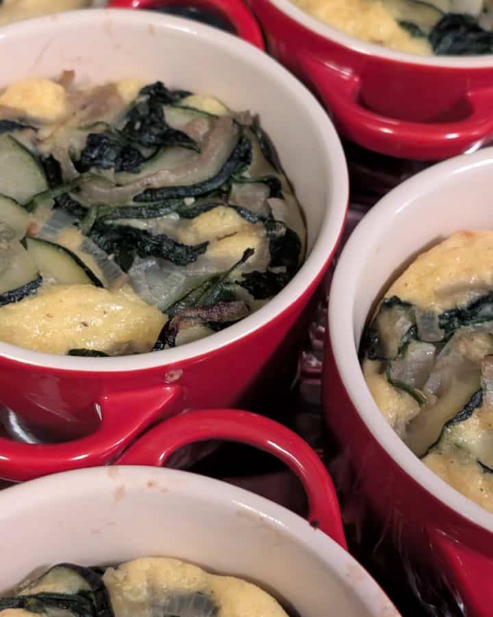 Individual sized Zucchini Gouda Bakes already baked in coquettes set on a rimmed baking sheet