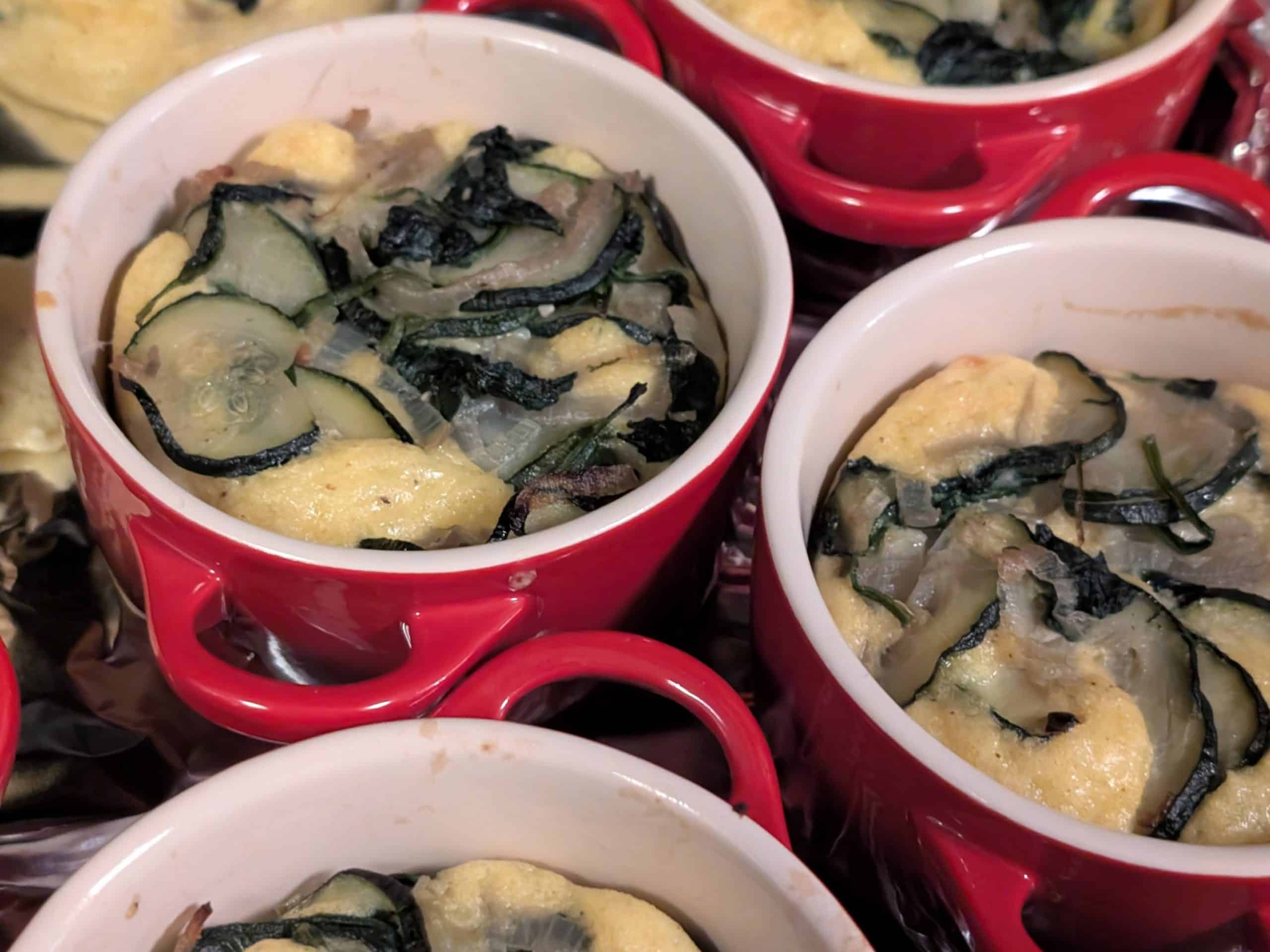 Individual sized Zucchini Gouda Bakes already baked in coquettes set on a rimmed baking sheet