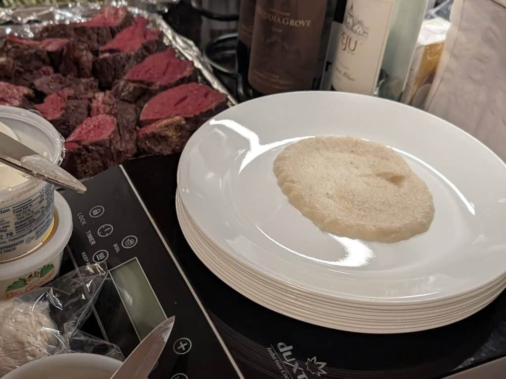 A plating station containing a large white plate with a large dollop of Turnip and Rosemary Purée ladled into the middle.