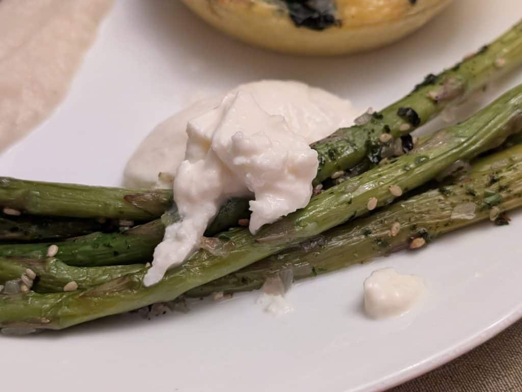 A close-up picture of Roasted Asparagus with Furikake and Burrata on a plate for service