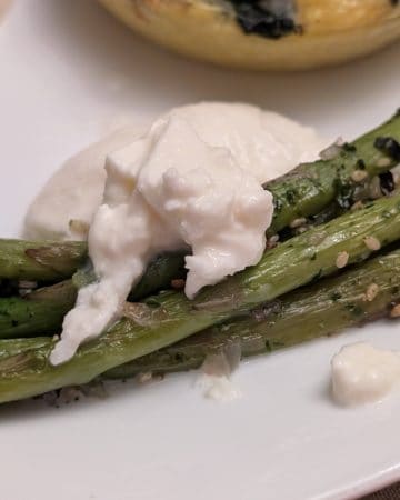 A close-up picture of Roasted Asparagus with Furikake and Burrata on a plate for service
