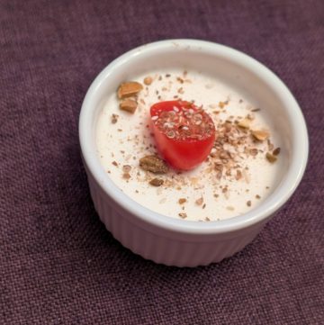 Savory Goat Cheese Panna Cotta in a small, white ramekin topped with Dukkah and a sliced grape tomato