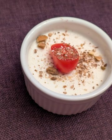 Savory Goat Cheese Panna Cotta in a small, white ramekin topped with Dukkah and a sliced grape tomato