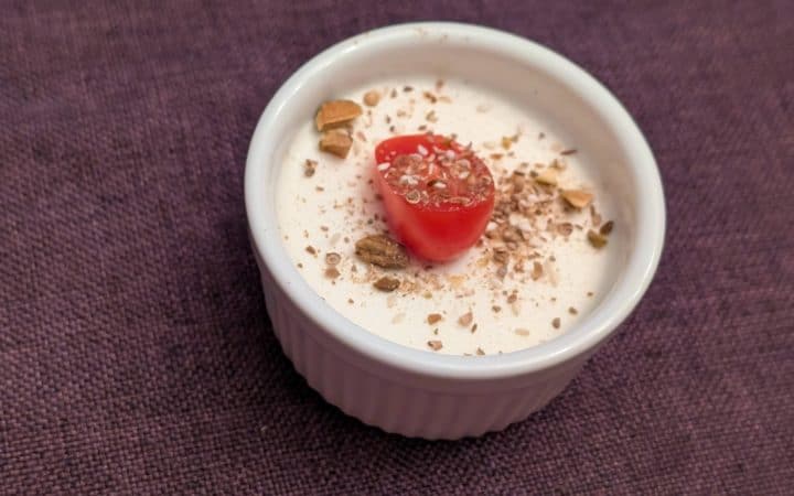 Savory Goat Cheese Panna Cotta in a small, white ramekin topped with Dukkah and a sliced grape tomato