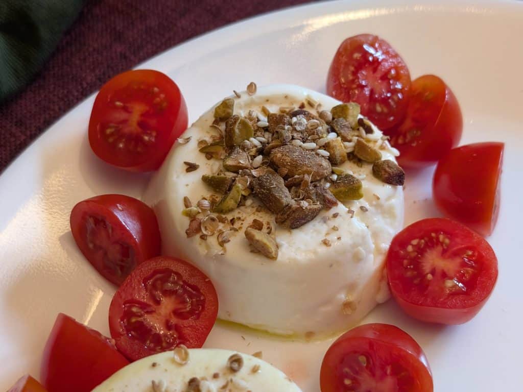 Savory Goat Cheese Panna Cotta on a plate topped with Dukkah and surrounded by sliced grape tomatoes