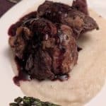 A plate containing a slice of beef tenderloin on a bed of Turnip and Rosemary Purée drizzled with a Blackberry Red Wine Reduction Sauce.