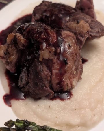 A plate containing a slice of beef tenderloin on a bed of Turnip and Rosemary Purée drizzled with a Blackberry Red Wine Reduction Sauce.