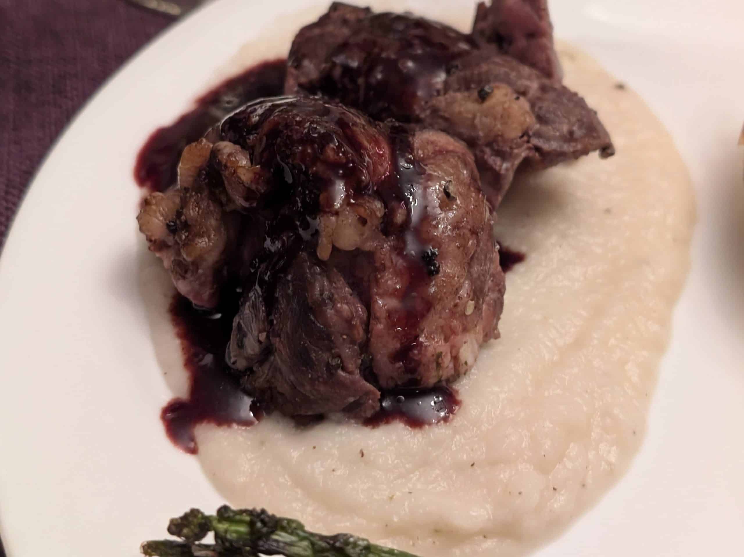 A plate containing a slice of beef tenderloin on a bed of Turnip and Rosemary Purée drizzled with a Blackberry Red Wine Reduction Sauce.