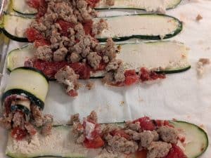 Zucchini planks covered in savory plant-based spread, fire roasted diced tomatoes, and ground chicken cooked with Pizza Masti Spice Blend, ready to roll up
