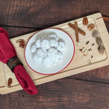 Spiced Cookie Balls on a plate on a tray next to cinnamon sticks, cloves, and shaved almonds