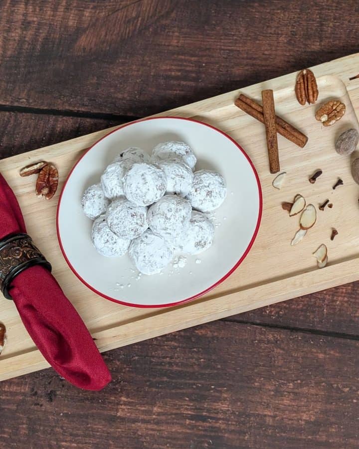 Spiced Cookie Balls on a plate on a tray next to cinnamon sticks, cloves, and shaved almonds