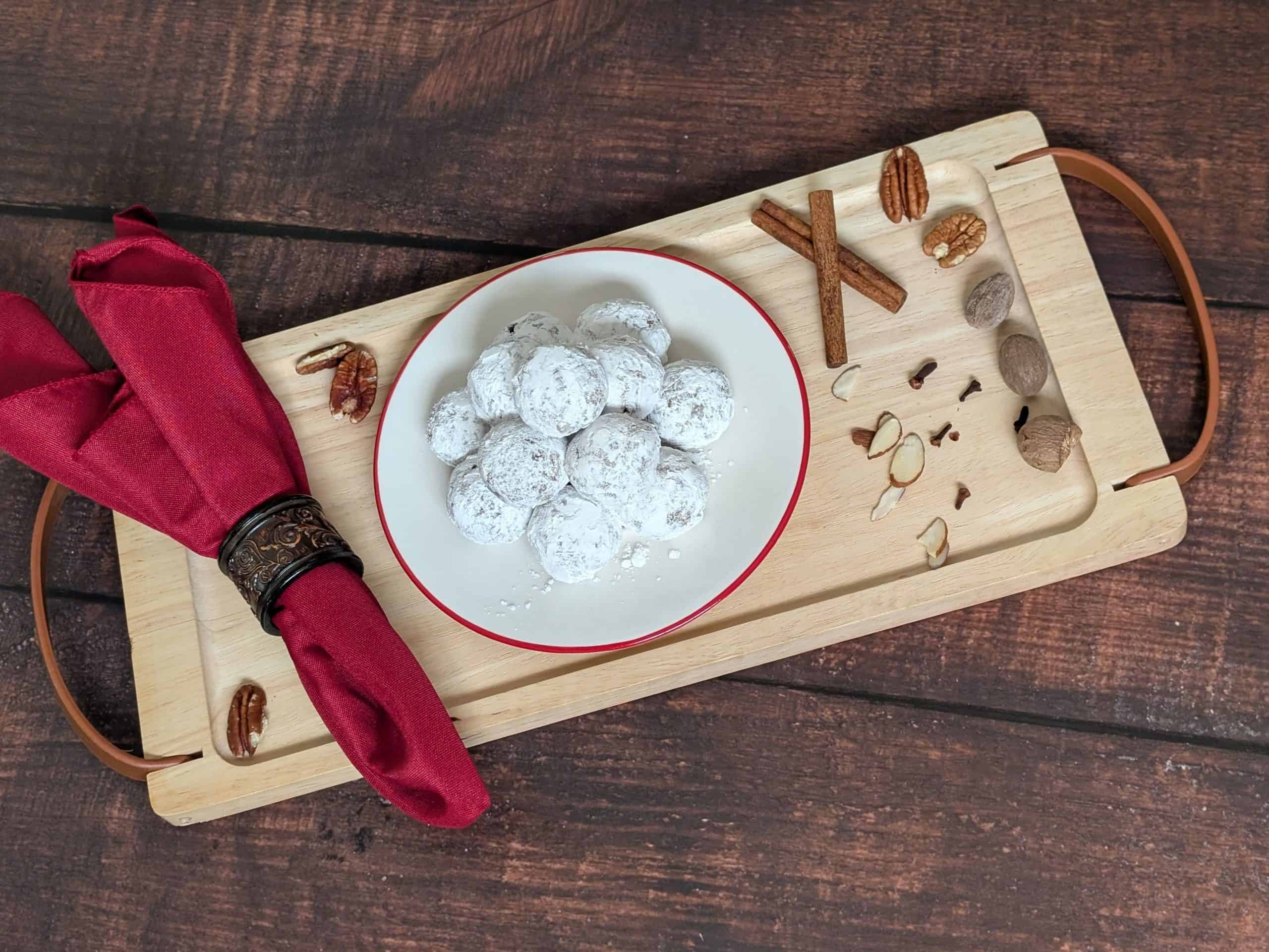 Spiced Cookie Balls on a plate on a tray next to cinnamon sticks, cloves, and shaved almonds
